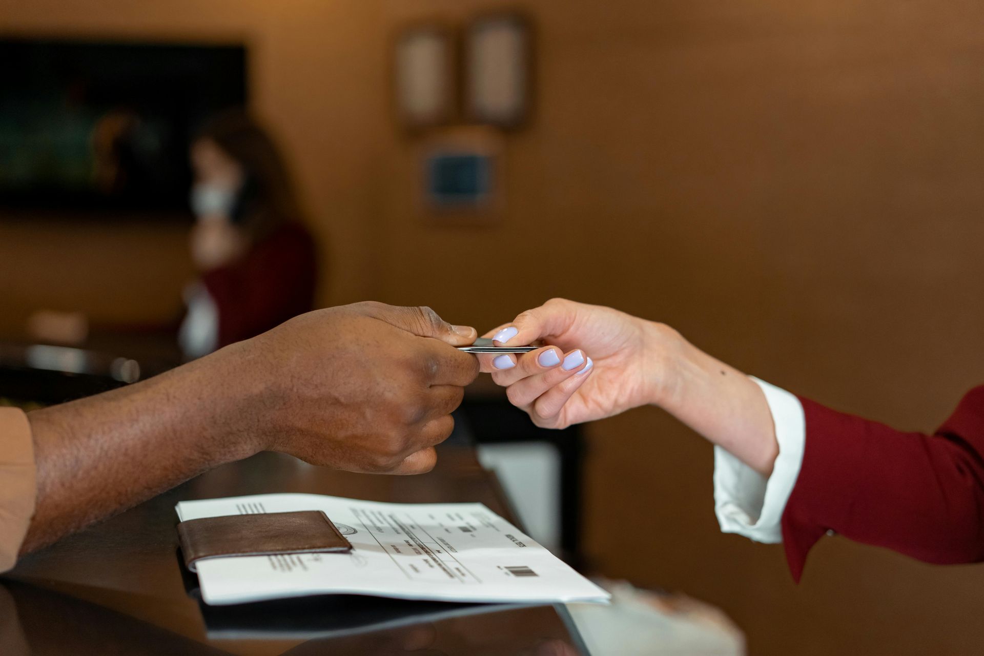 A person hands a key card to a receptionist over a hotel check-in counter.