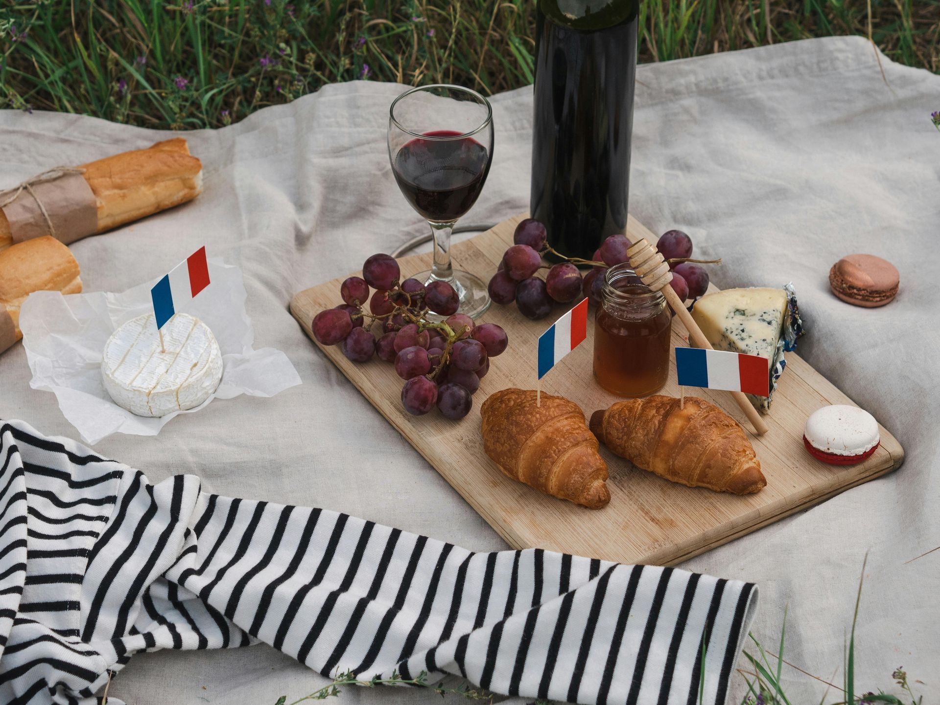 Picnic featuring French food and wine, with a striped shirt, baguette, and French flags.