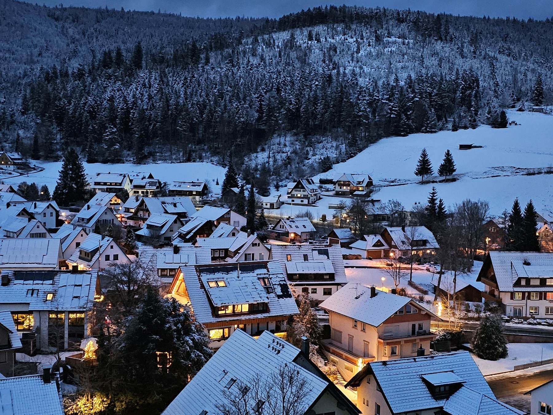 Verschneites Obertal bei Baiersbronn im Schwarzwald in der Abenddämmerung mit beleuchteten Häusern im Winter