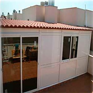 Un solárium o cerramiento con estructura de aluminio blanco y puertas corredizas de vidrio en una terraza en la azotea con techo de tejas.