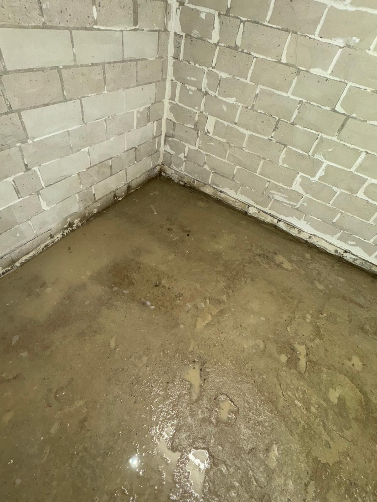 Wasser auf dem Betonboden in der Ecke eines Raums mit unfertigen Ziegelsteinwänden.