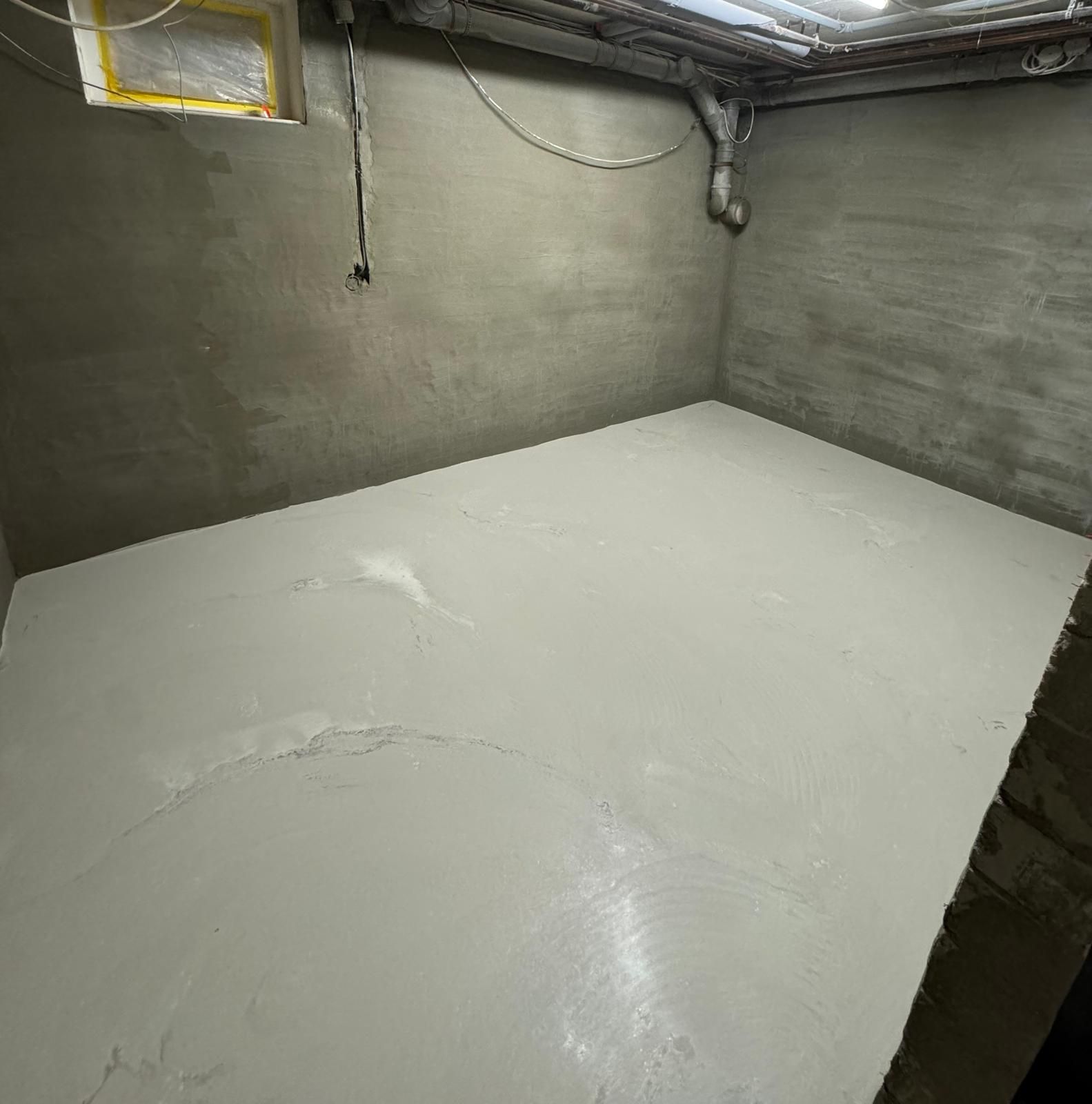 Leerer Raum mit frisch gegossenem, hellem Betonboden und grauen Wänden.