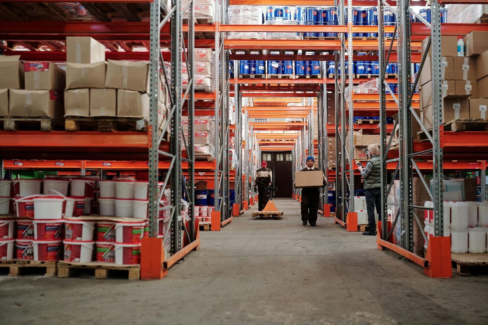 Interior del almacén con trabajadores moviendo cajas y mercancías en estantes.