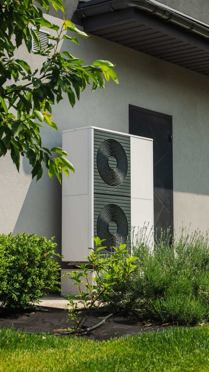 Unité de pompe à chaleur blanche sur la façade d'un bâtiment, près de la végétation.