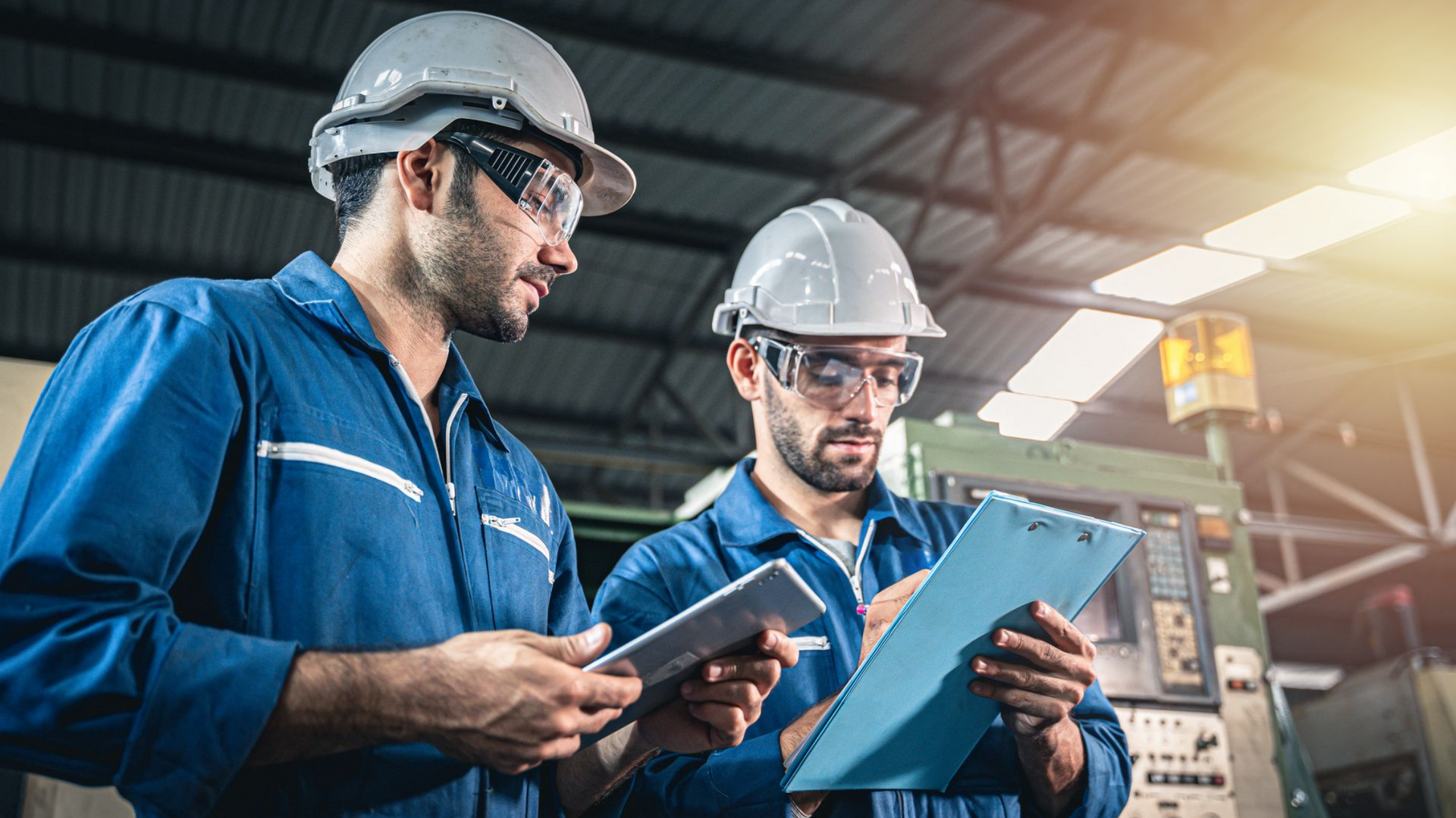 Deux ouvriers en combinaisons bleues et casques de chantier examinent des documents dans une usine.