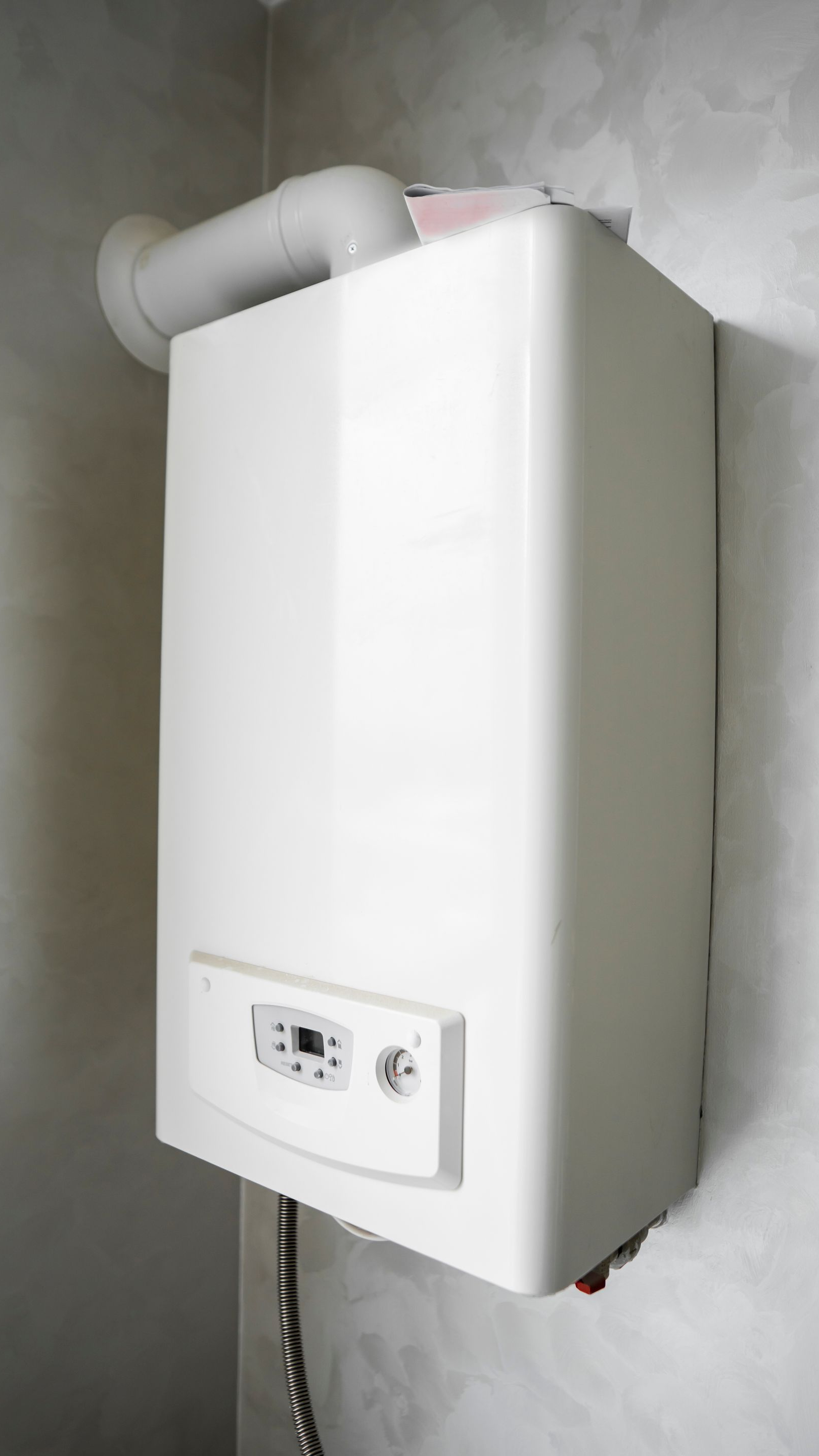 Chaudière murale blanche avec affichage numérique et tuyau d'évacuation.