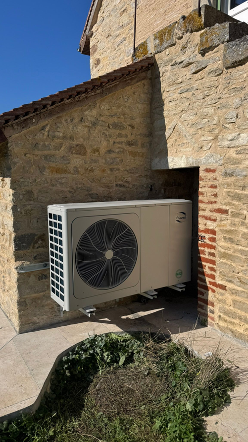 Unité de climatisation installée sur un bâtiment en pierre beige, se détachant sur un ciel bleu, avec quelques arbustes verts.