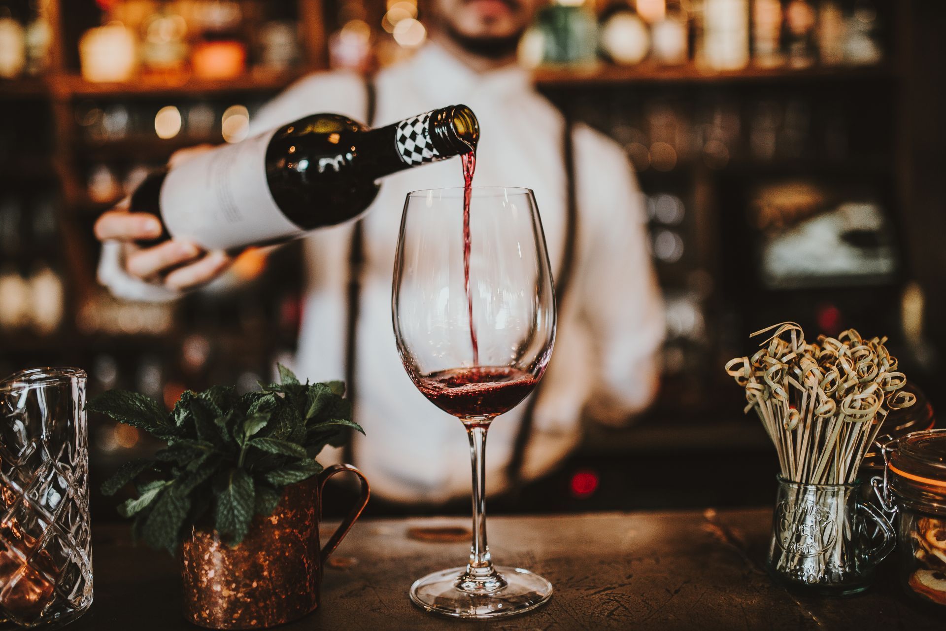 Bartender pours red wine into a glass at a bar.