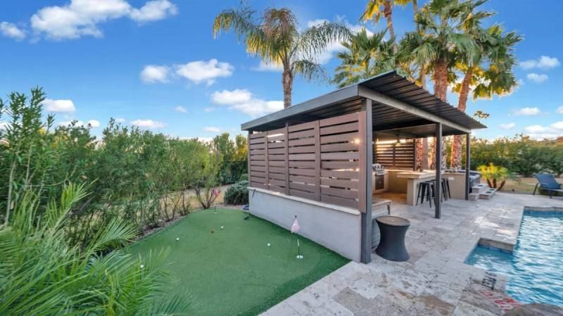 Outdoor kitchen with putting green and pool in a sunny setting.