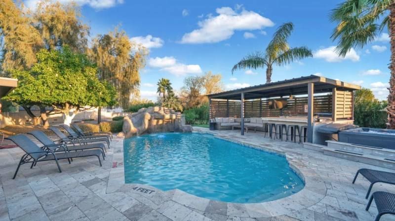 Pool with waterfall, loungers, gazebo with bar, palm trees, sunny day.