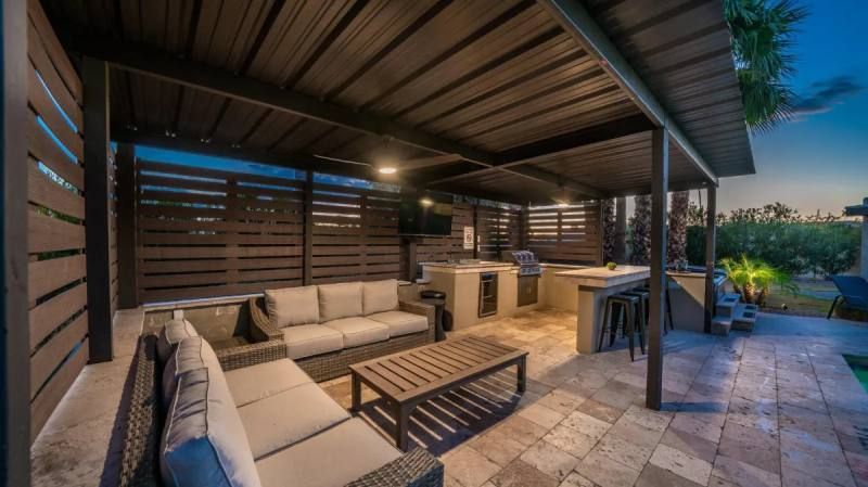 Outdoor kitchen and lounge area with seating, grill, and overhead shade structure.