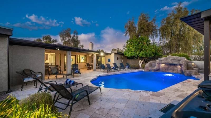Pool area with lounge chairs, blue water, and a rock waterfall feature at dusk.