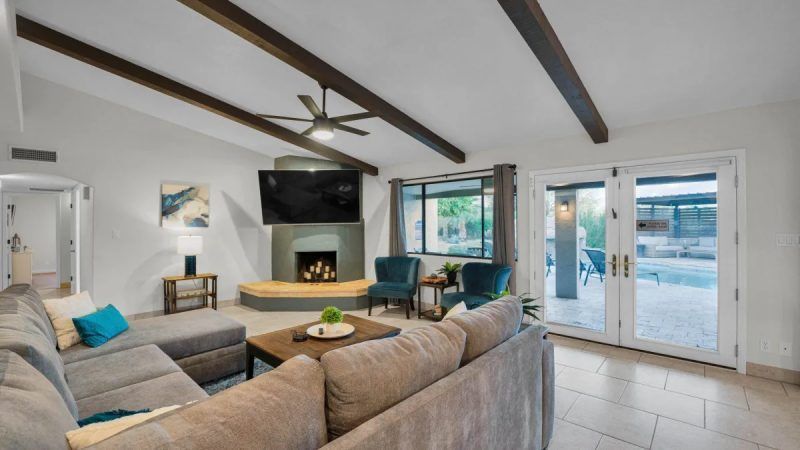 Living room with gray sectional, fireplace, TV, and pool view through glass doors.