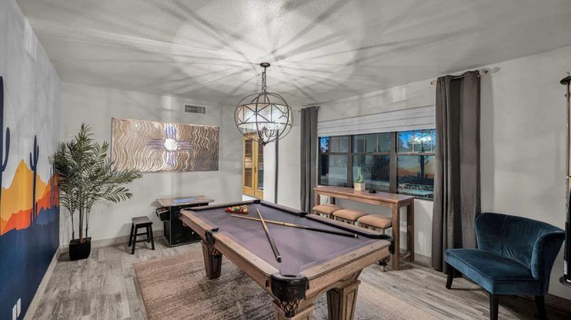 Pool room with a pool table, dark blue accent chair, and a large window with shades.