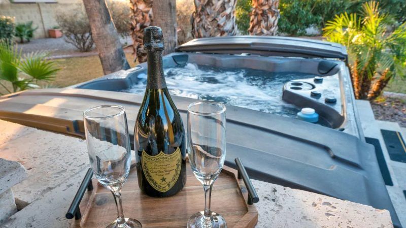 Champagne bottle and flutes on a tray beside a bubbling hot tub outdoors.