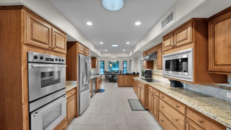 Long kitchen with wood cabinets, stainless steel appliances, and beige tile floor.