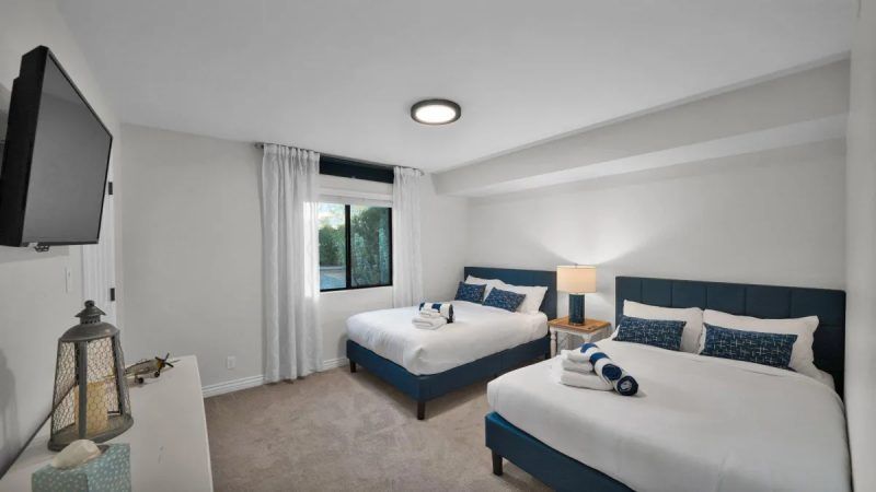 Two beds in a room, navy blue headboards, white linens, window, and TV.