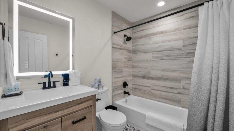 Bathroom with white countertop, wooden cabinet, tiled wall, and white bathtub.