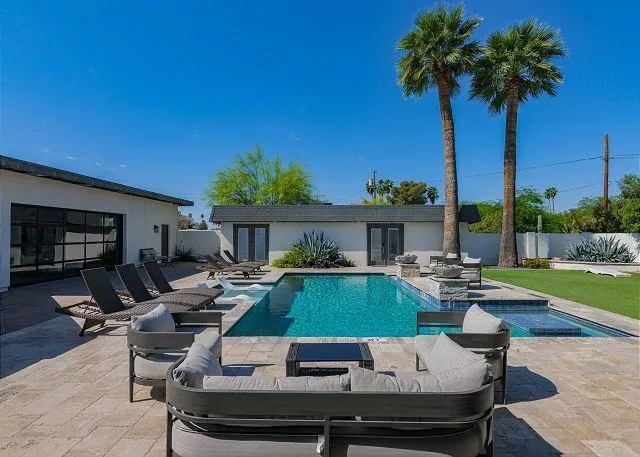 Backyard with a pool, lounge chairs, and palm trees under a blue sky.