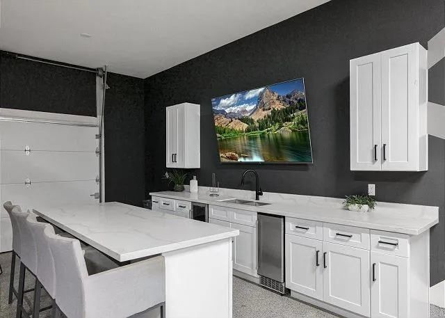 Modern kitchen with white countertops and cabinets, black wall, and a mounted TV.
