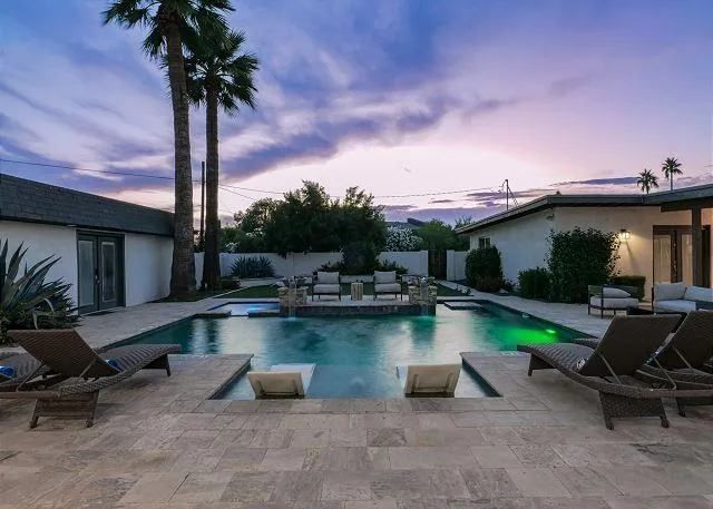 Backyard pool at sunset with lounge chairs and palm trees.