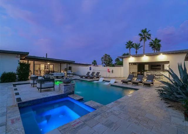 Pool area at dusk with pool, hot tub, lounge chairs, bar, and palm trees.