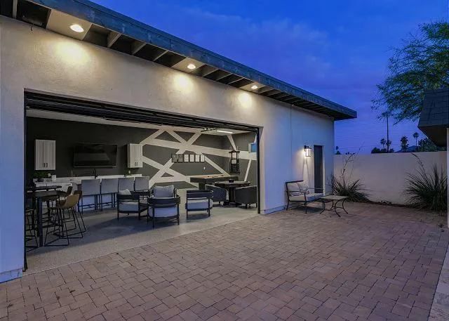 Patio with open garage door revealing a bar and seating area. Brick patio with overhead lighting.