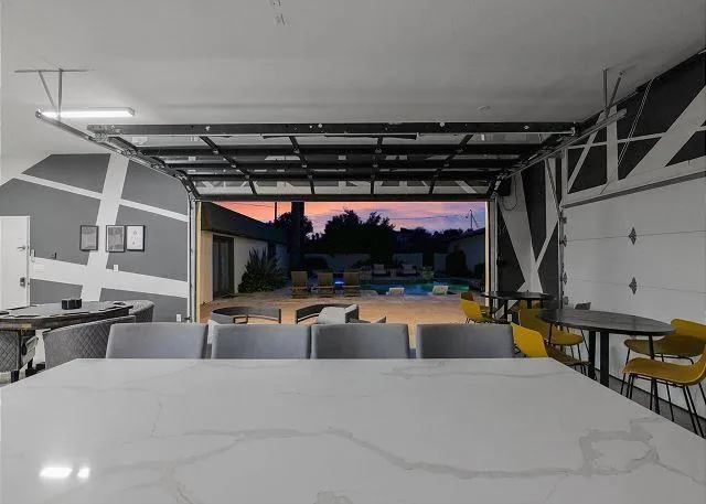 Garage open to a backyard with pool; long table and chairs in foreground, sunset in the background.