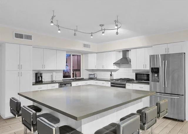 Modern white kitchen with island, stainless steel appliances, and seating.
