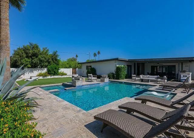 Backyard with pool, lounge chairs, and house on a sunny day.