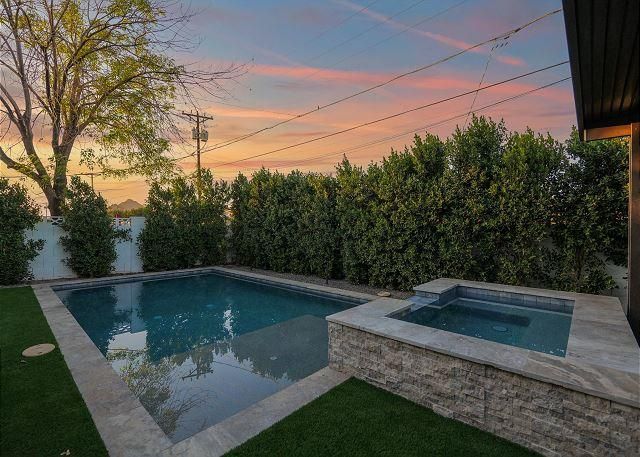 Backyard pool and spa with green hedges and a sunset sky.