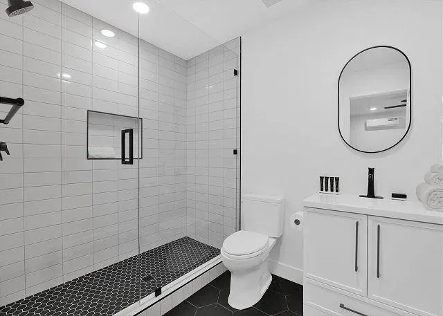 Modern bathroom with a tiled shower, white vanity, and oval mirror.