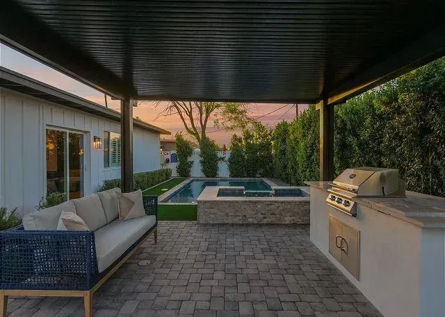 Patio with sofa, outdoor kitchen, pool, and pergola with black accents.