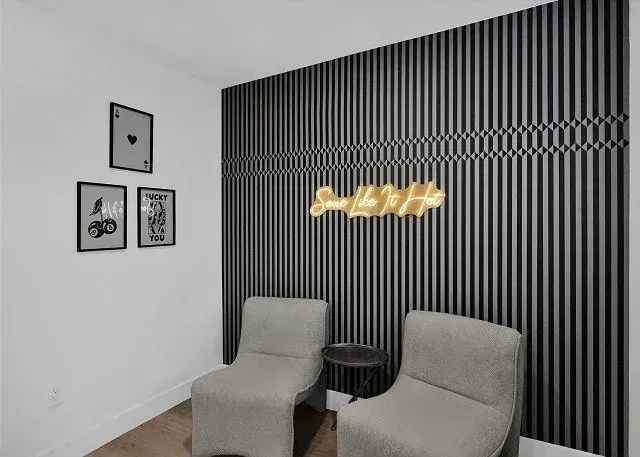 Two gray chairs face a textured wall with a neon sign and framed art.