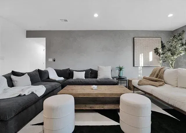 Living room with gray walls, dark gray sectional, white sofa, wooden coffee table, and black and white rug.