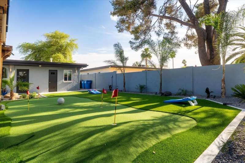 Backyard with putting green, flags, and building. Green turf with blue sky.