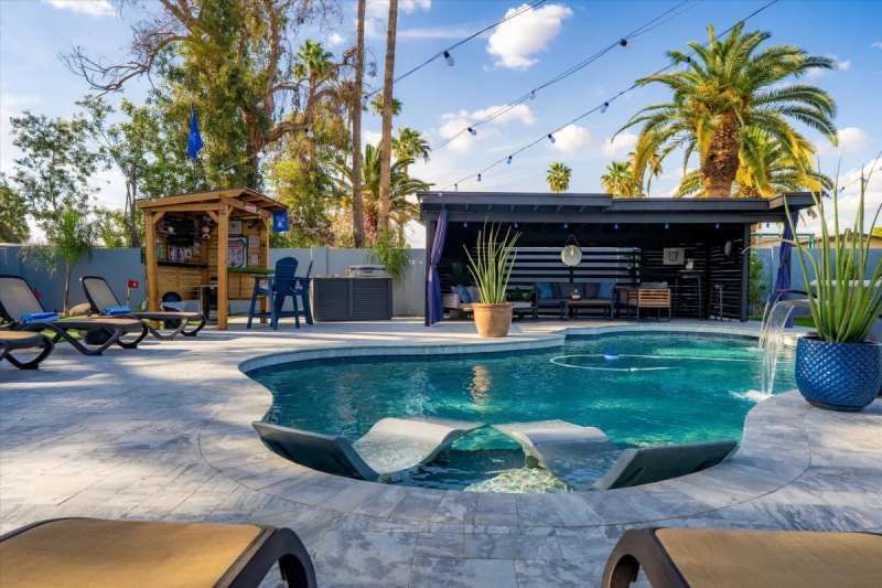 Poolside oasis with pool, lounge chairs, bar, and seating area under a pergola.