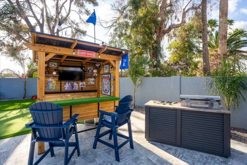 Backyard bar area with TV, seating, and grill. Blue flag flies above.