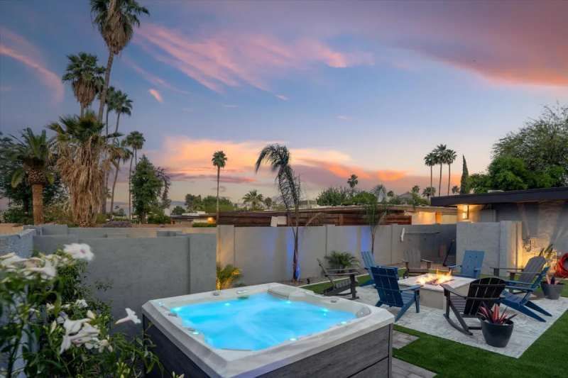 Hot tub and lounge chairs on a patio at sunset with palm trees.