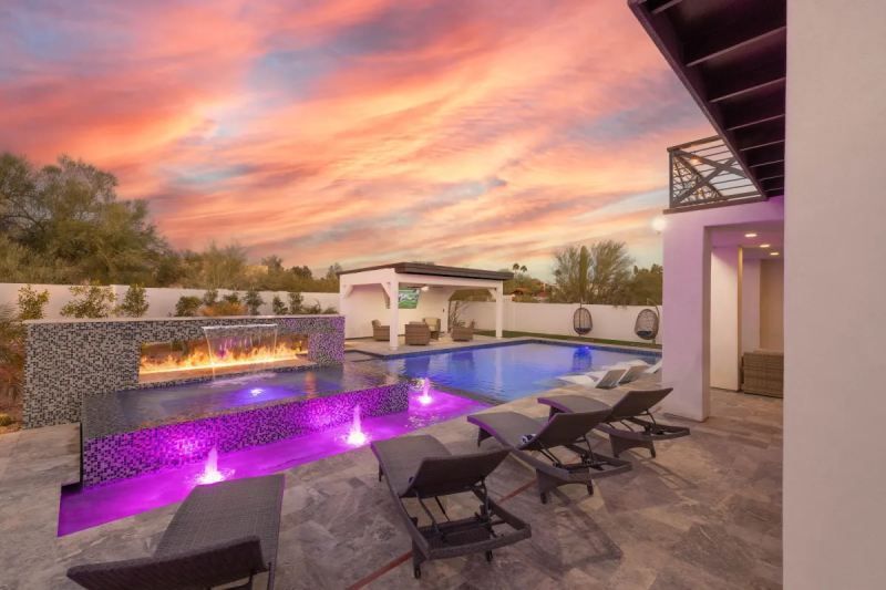 Pool and patio at dusk; fire feature, purple lights, lounge chairs, and a sunset sky.