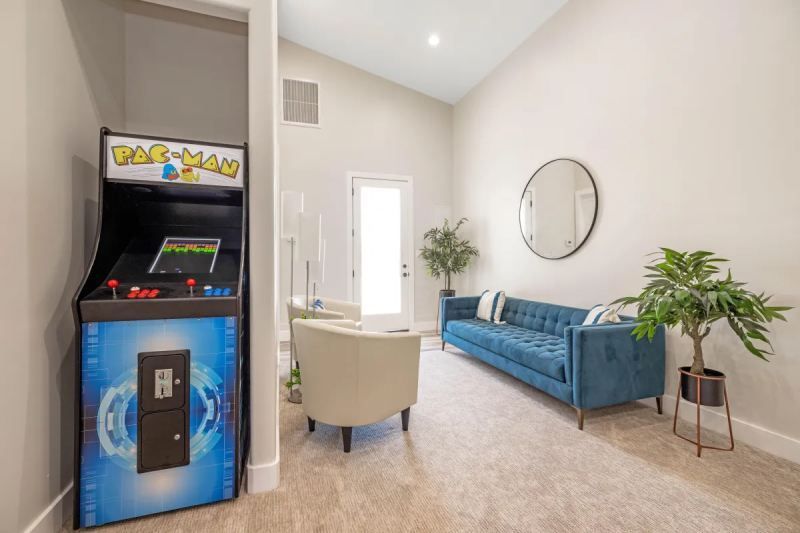 Arcade game in a living room with blue sofa, armchair, and plants.
