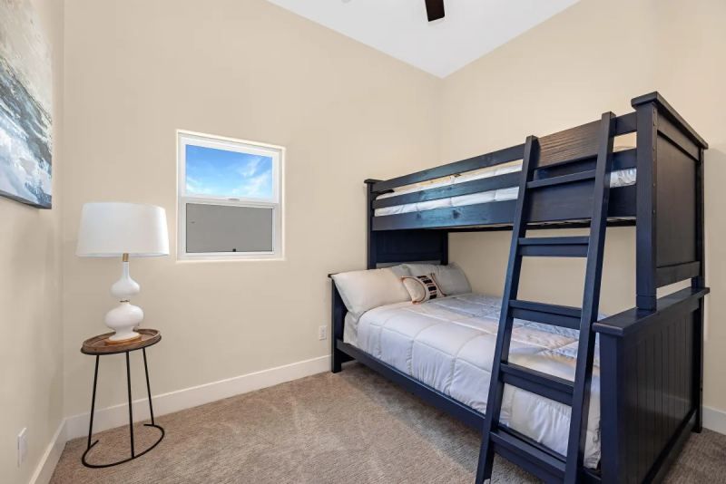 Bedroom with blue bunk bed, small window, side table with lamp, neutral walls and carpet.