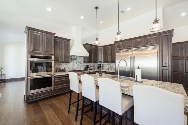 Elegant kitchen with dark cabinets, stainless steel appliances, and a granite island with white bar stools.