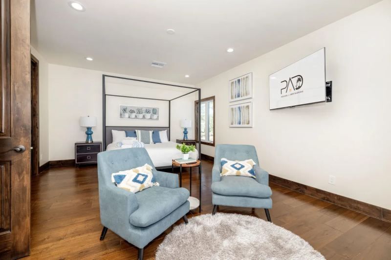 Bedroom with blue armchairs, canopy bed, wooden floors, TV, and decorative art.