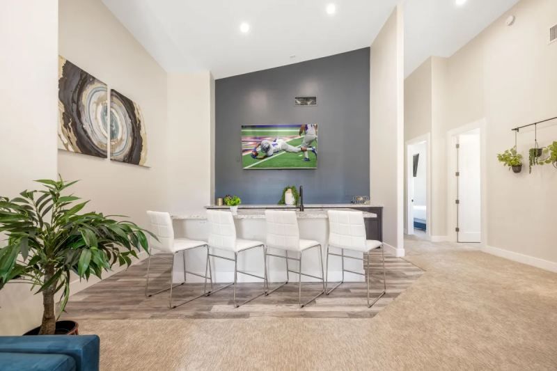 Modern entertainment space with bar seating, TV, art, and neutral tones.