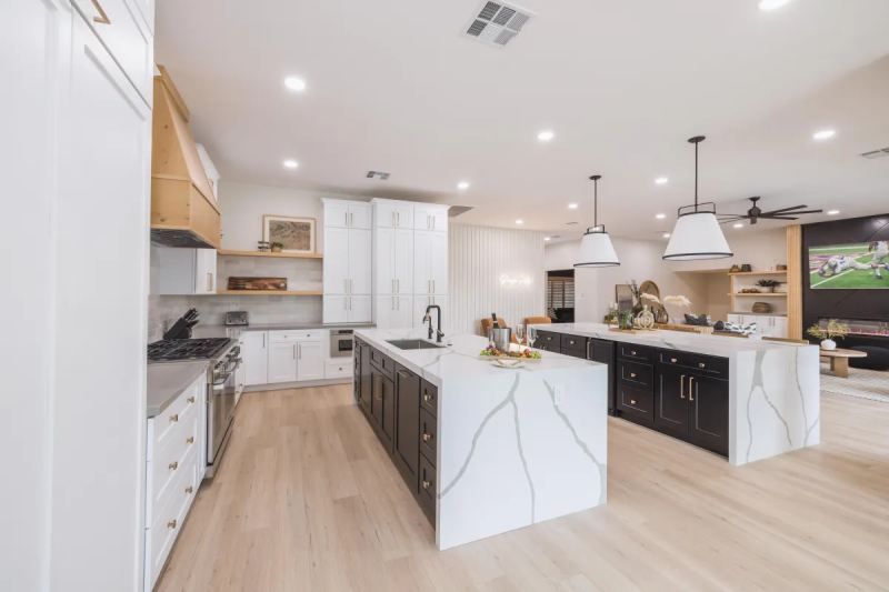 Modern kitchen with white and dark wood cabinets, large island, light wood floors, and pendant lighting.
