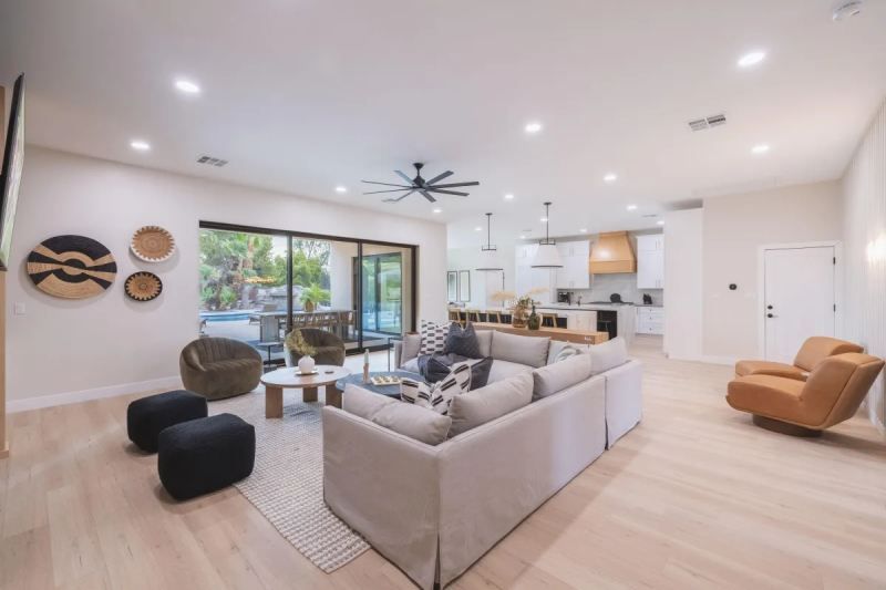 Spacious, modern living room with light wood floors, neutral walls, and large sliding glass doors leading to a pool.
