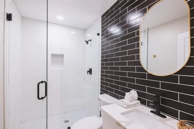 Modern bathroom with black brick accent wall, white fixtures, and a glass shower.