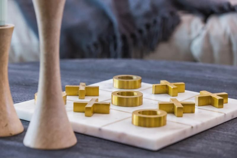 Tic-tac-toe game with gold X's and O's on a white marble board, next to decorative wooden candlesticks.