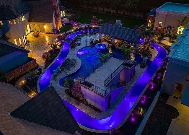 Night view of a luxurious backyard with pool and waterslide illuminated in blue.